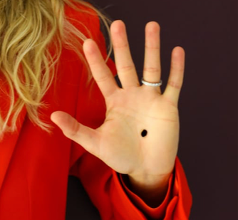 Une femme a dessiné un point noir sur la paume de sa main. Symbole des violences conjugales.