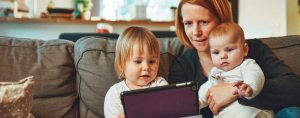 Une maman et ses deux enfants regardent une tablette installés dans leur canapé.