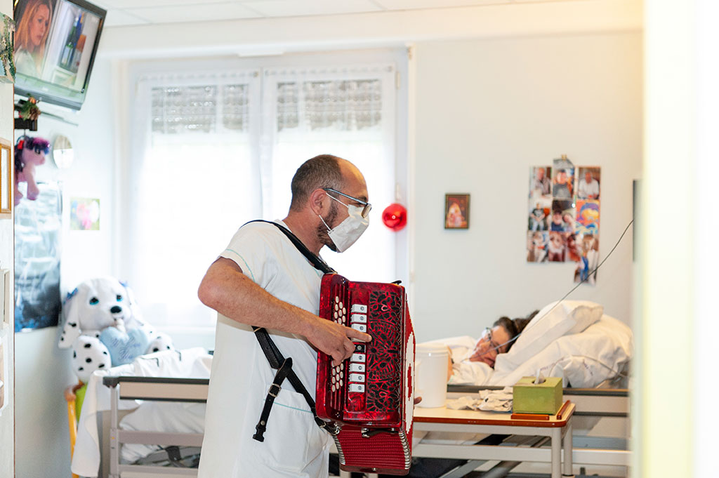 Un animateur joue de l'accordéon dans la chambre d'une résidente de l'hôpital de Boucicaut.